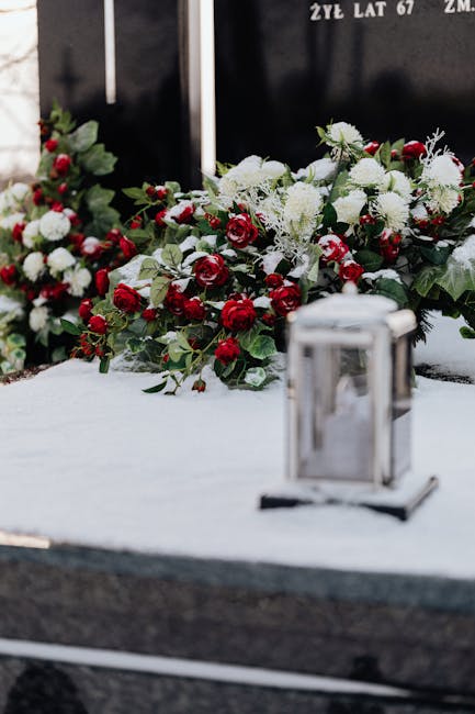 A floral tribute composed of white chrysanthemums and red roses, arranged with green foliage, resting on a white cloth at a memorial site. The bouquet is laid out on a flat surface with a metallic lan