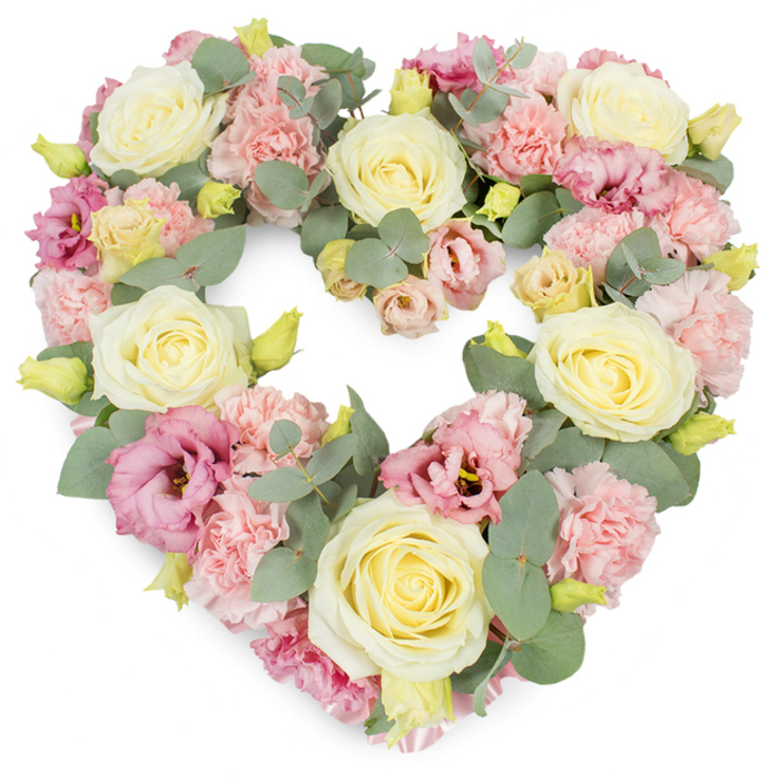 A lush heart-shaped tribute dominates the frame, its design a careful balance of soft colour, abundant texture, and graceful form. The outline of the heart is clear and smooth, formed by a dense mass of flowers in cream, pale yellow, and varied pinks, all supported by subtle greenery. Large, fully opened cream and buttery-yellow roses are positioned as anchors throughout the wreath, their velvety petals spiralling in tight, elegant whorls that bring a sense of calm to the arrangement. Between them, light pink carnations fill the spaces, their finely ruffled petals packed closely together to create a plush, almost quilted effect that softens every line. Threaded through this pastel foundation are blooms of deeper pink and mauve lisianthus, some fully open and some partially unfurled, their softer, more relaxed petals adding a hint of movement and emotional depth. Eucalyptus foliage, in a cool, silvery-green tone, winds delicately through and around the flowers, the rounded leaves tracing the heart's edges and enhancing the overall shape without overwhelming it. Small yellowish-green buds peek from between petals and leaves, suggesting buds just ready to open, and hinting at the freshness expected from same-day arrangements created by Flowers Kenton. The white background around the wreath allows the pastel tones to stand out clearly, giving the impression of lightness despite the densely packed design. The mood is gentle and reflective, ideally suited for funerals, cremation services, or remembrance gatherings across Kenton, from quiet suburban streets to local churches, where families wish to express sympathy, gratitude, and unwavering love through a serene floral heart.